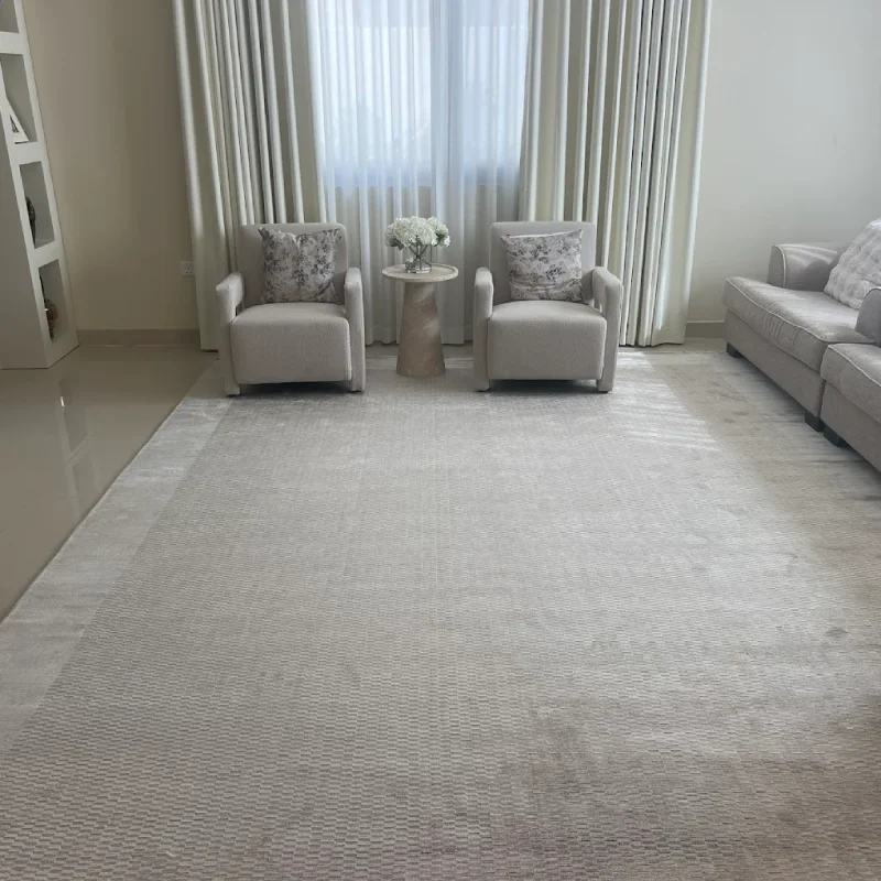 A beige-colored living room with a large, light-colored rug covering most of the floor. Two matching armchairs with floral patterned throw pillows