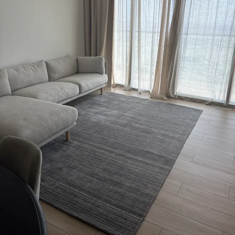 A contemporary living space featuring a light gray sectional sofa placed against a white wall. The room has light wood-patterned flooring