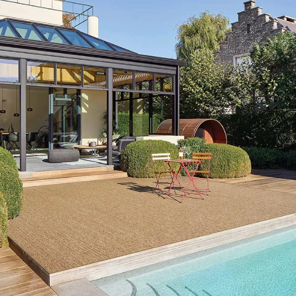 A view of a modern backyard patio with a swimming pool. The patio area is covered with a textured, tan-colored outdoor rug or carpeting,