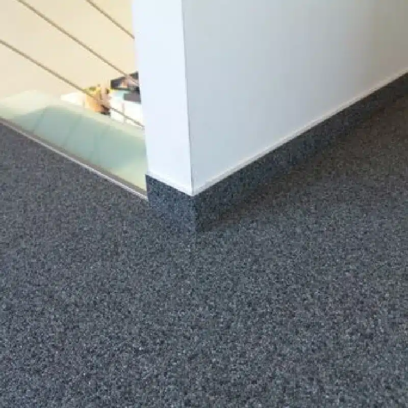 Dark gray speckled stone carpet flooring next to a white wall (1)