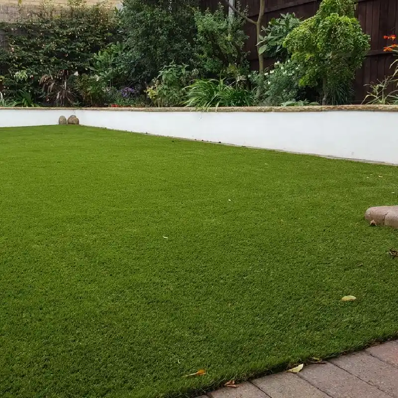 lush, bright green artificial grass lawn bordered by a low white wall with natural foliage above